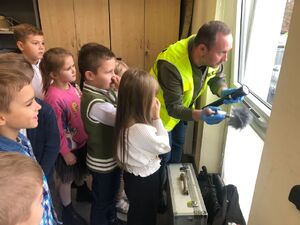 policjanci w żółtych kamizelkach pokazują grupie dzieci zabezpieczanie śladów