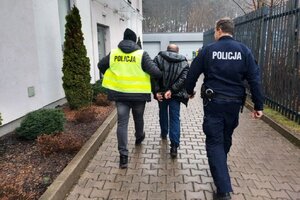 Dwóch policjantów prowadzi w środku zatrzymanego mężczyznę