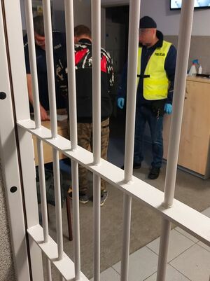 Policjant w żółtej kamizelce prowadzi zatrzymanego mężczyznę.