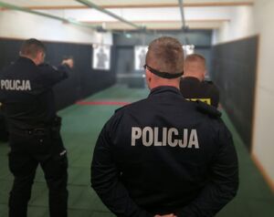 Policjanci odwróceni tyłem celują w obiekt ustawiony na strzelnicy.