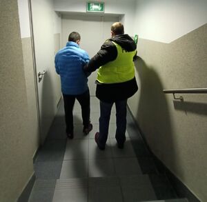 Policjant w żółtej kamizelce prowadzi zatrzymanego mężczyznę.