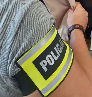 Na ramieniu policjanta założona opaska z napisem Policja.