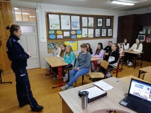 Policjantka stoi na środku klasy gdzie przed nią są ustawieni w ławkach uczniowie.