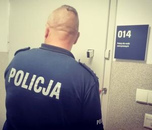 Policjant odwrócony tyłem stoi przy metalowych drzwiach.