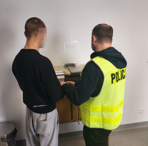 zatrzymany mężczyzna stoi przy policjancie w żółtej kamizelce z napisem policja