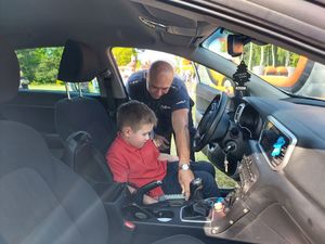 Policjant pochylony nad chłopcem siedzącym na miejscu kierowcy w radiowozie.