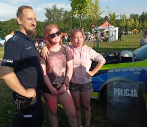 Policjant stoi obok dwóch nastolatek obsypanymi kolorowymi farbami.