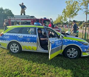 Policjantka siedzi w radiowozie na miejscu pasażera, obok radiowozu stoi wóz strażacki.