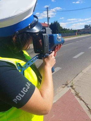 Policjantka odwrócona bokiem przykłada niebieskie urządzenie do pomiaru prędkości do twarzy.