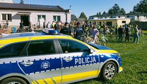 Radiowóz policyjny zaparkowany, obok stoi dwójka policjantów a przed nimi grupa ludzi z rowerami.