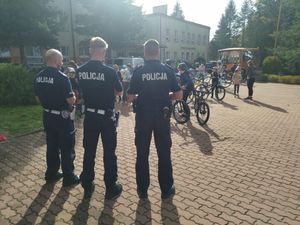 Trzech policjantów stoi na placu gdzie ustawiają się dzieci z rowerami.