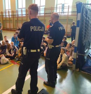 Dwóch policjantów stoi na sali, przed nimi siedzą dzieci.