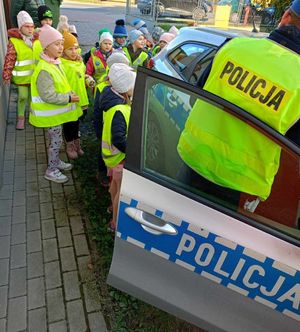Policjant stoi przy radiowozie przy którym stoją małe dzieci.