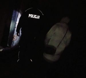 Policjant świeci latarką w ciemnym miejscu , obok niego siedzi kobieta.