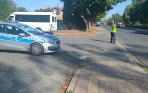 Policjant stoi przy drodze i mierzy prędkość.