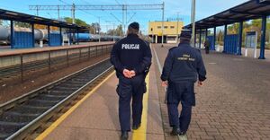 Policjant i strażnik kolejowy idą wzdłuż torów.