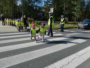 Dwóch policjantów stoi przy przejściu dla pieszych przez które przechodzą małe dzieci.