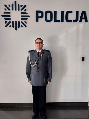 Policjant w galowym mundurze stoi przy ścianie na której widnieje napis Policja.
