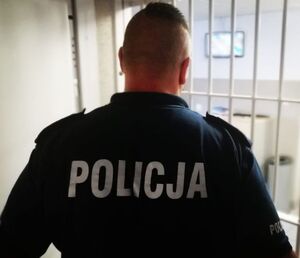 Policjant stoi odwrócony tyłem przy okratowanych drzwiach.
