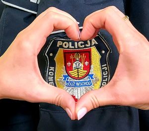 Dłonie ułożone w kształcie serca przy naszywce na mundurze z napisem Policja Łódź Wschód.