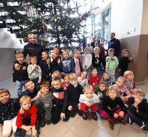 Policjant i policjantka stoją z grupą małych dzieci przy dużej choince.