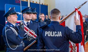 Policjant stoi przed flagą polski i ślubuje z uniesioną prawą ręką.