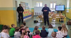 Dwóch policjantów stoi na środku sali, w której siedzą dzieci.