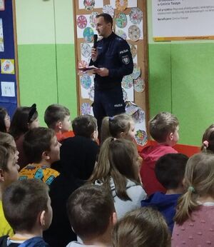 Policjant stoi na środku sali, w której siedzą dzieci.