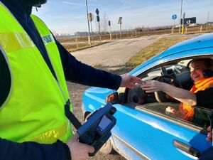 Policjant podaje kobiecie siedzącej za kierownicą zawieszkę w kształcie serduszka.