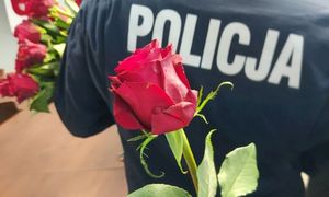 Czerwona róża na tle granatowego munduru z napisem Policja.