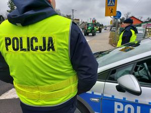 Policjanci stoją przy radiowozie, obok drogi którą jadą traktory.