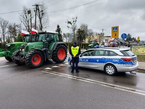 Policjanci stoją przy radiowozie, obok drogi którą jadą traktory.