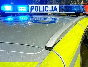 Dach radiowozu policyjnego z sygnalizatorem z napisem policja i migającym niebieskim światłem.