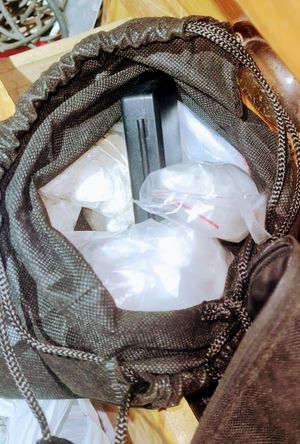 Narkotyki w postaci białego proszku zawinięte w folię i ukryte w czarnej torbie.