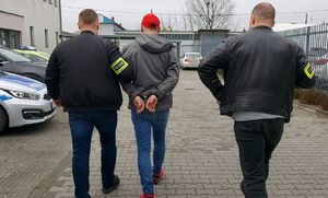 Dwóch policjantów prowadzi zatrzymanego mężczyznę.