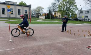 Dziecko jadące na rowerze, za nim idzie policjant.