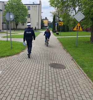 Dziecko jadące na rowerze, za nim idzie policjant.