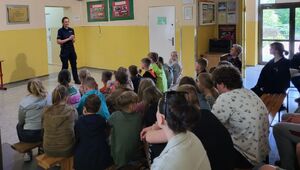 Policjantka stoi na środku sali, w której na ławkach przed nią siedzą młodzi ludzie.