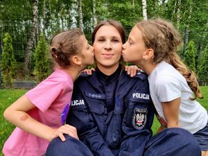 Dwie dziewczynki całują w policzek siedzącą pomiędzy nimi policjantkę.