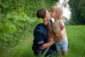 Policjantka kuca przy małym chłopcu, całują się w usta.