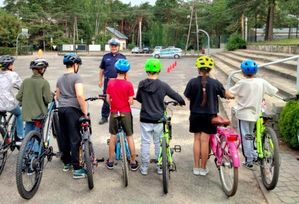 Policjant stoi przed grupą dzieci, które stoją przy rowerach i mają na głowie kaski ochronne.