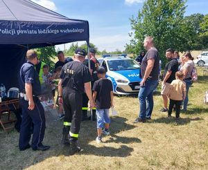 Przy policyjnym granatowym namiocie stoją policjanci i zainteresowane osoby.