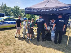 Przy policyjnym granatowym namiocie stoją policjanci i zainteresowane osoby.