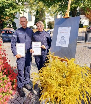 Policjantka i policjant stoją na placu i trzymają w dłoniach podziękowania.