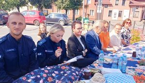 Policjant i policjantka siedzą w grupie osób na terenie placu.