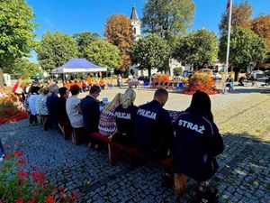 Policjant i policjantka siedzą w grupie osób na terenie placu.