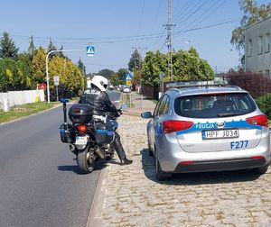 Policjant na motocyklu stoi przy radiowozie.