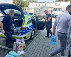 Policjanci pakują rzeczy do bagażnika radiowozu.