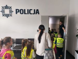 Policjantka stoi przy grupie dzieci, które mają na sobie żółte kamizelki.