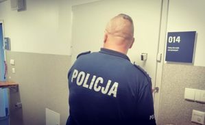 Policjant stoi przy drzwiach metalowych do pomieszczenia dla osób zatrzymanych.